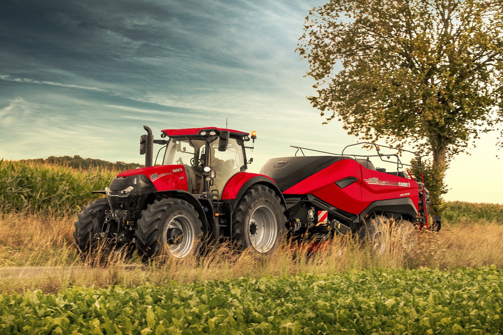 Röd traktor - balpress på väg genom fält